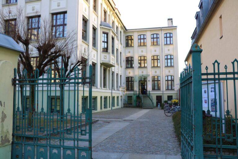 Innenhof eines historischen Gebäudes mit offenem grünen Tor, Treppe am Eingang und mehreren Fahrrädern.