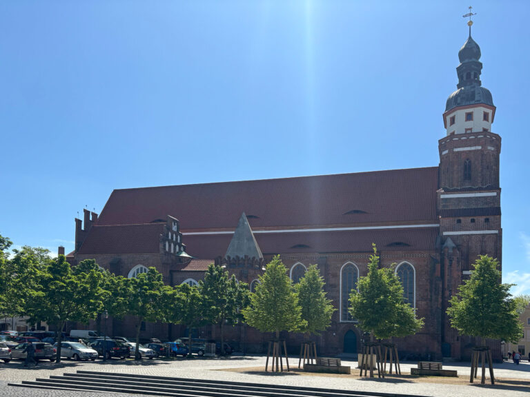 Die Oberkirche St. Nikolai in Cottbus mit rotem Dach, Backsteinturm und blauem Himmel über dem Platz.