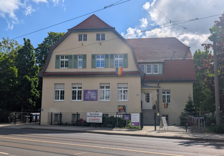 Das Haus in der Thiemstraße 55 trägt das Schild „Lila Villa“ und Regenbogenfahnen; davor stehen Hinweise zu Büroräumen und Beratungsräumen.