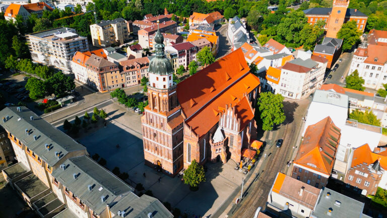 Luftaufnahme der Oberkirche St. Nikolai mit rotem Dach, umgeben von Altstadthäusern und viel Grün in Cottbus.