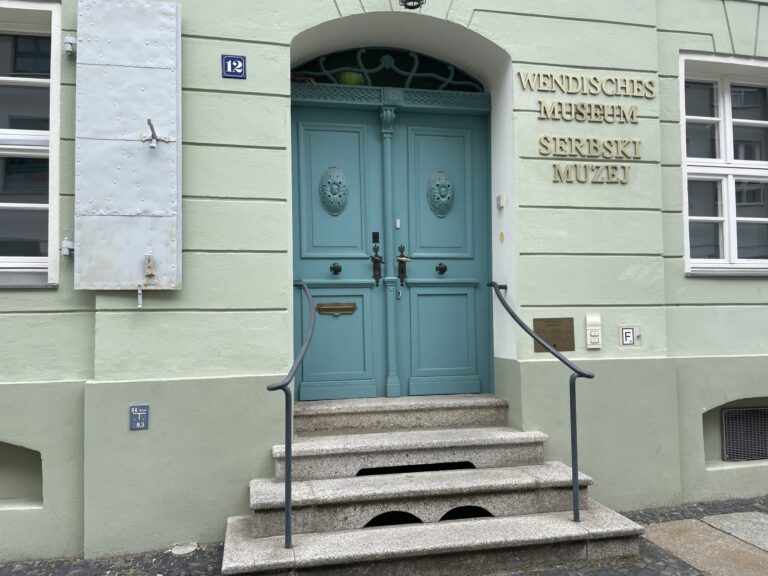 Die hellgrüne Fassade des Wendischen Museums zeigt eine blaue Doppeltür und den Schriftzug „Wendisches Museum Serbski Muzej“.