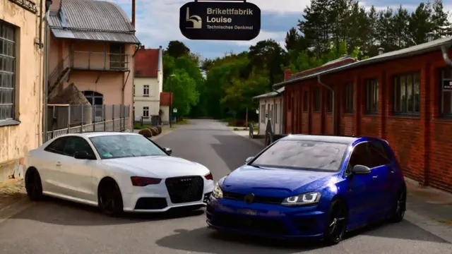 Vor dem Schild „Brikettfabrik Louise Technisches Denkmal“ stehen ein weißes Coupé und ein blaues Kompaktfahrzeug.