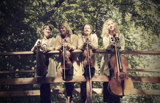 Vier Musikerinnen lehnen an einem Holzgeländer im Grünen und halten ihre Streichinstrumente unter dichtem Baumdach.