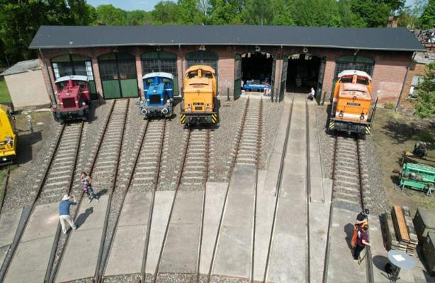 Vor dem Lokschuppen stehen mehrere Lokomotiven in verschiedenen Farben auf den Gleisen des Bahnbetriebswerks.
