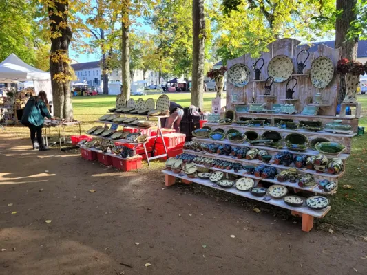 Auf dem Töpfermarkt stehen Tische mit bemalten Tellern, Schalen und Keramikgefäßen unter Bäumen auf einem Parkgelände.