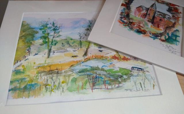 Zwei gerahmte Aquarellzeichnungen zeigen eine farbige Landschaft mit Hügeln und ein kleines Hausmotiv.