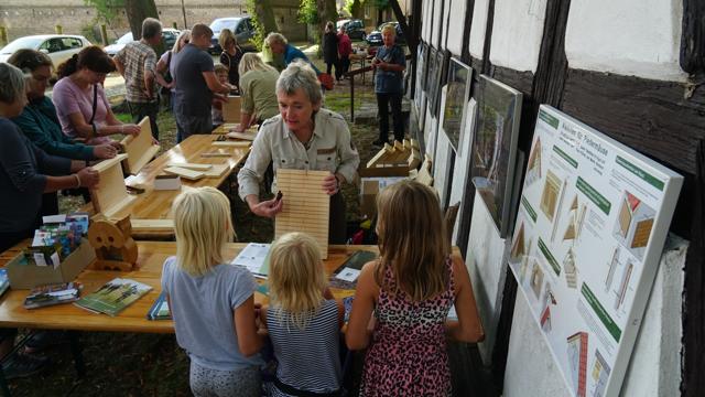 Mehrere Erwachsene und Kinder bauen an Tischen an der Fachwerkkirche Groß Schauen Holzquartiere für Fledermäuse zusammen.