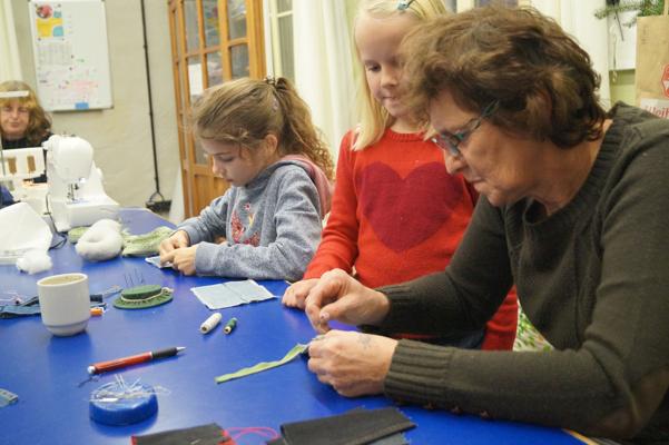 Drei Kinder und eine Betreuerin arbeiten an einem blauen Tisch mit Nähmaschine, Stoffstreifen und kleinen Bastelmaterialien.