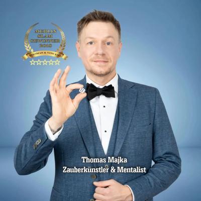 Ein Zauberkünstler im blauen Anzug und mit Fliege zeigt eine OK-Geste; auf dem Bild steht „Zauberkünstler & Mentalist“.