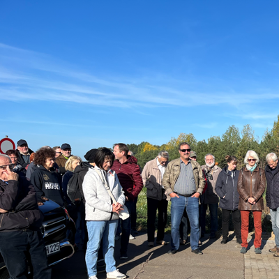 Mehrere Besucherinnen und Besucher stehen auf einem Weg am Cottbuser Ostsee unter blauem Himmel.