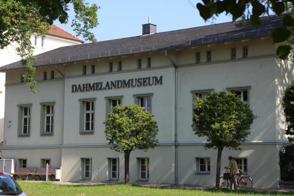 Am hellen Museumsgebäude steht der Schriftzug DAHMELANDMUSEUM, davor wachsen zwei Bäume und ein Fahrrad.