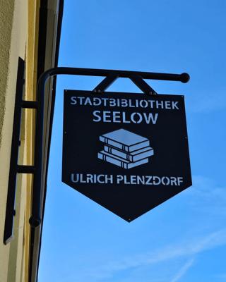 Das schwarze Hängeschild zeigt Stadtbibliothek Seelow, ein Bücherstapel-Symbol und den Schriftzug Ulrich Plenzdorf.