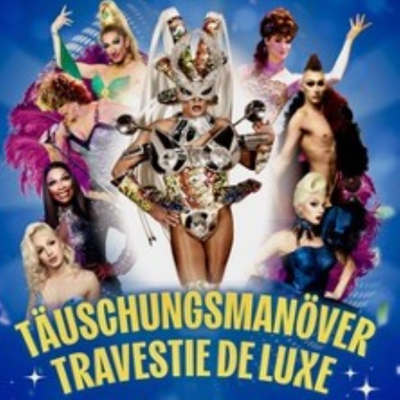 Mehrere Drag-Performer in glitzernden Kostümen vor blauem Hintergrund, unten steht „Täuschungsmanöver Travestie Deluxe“.