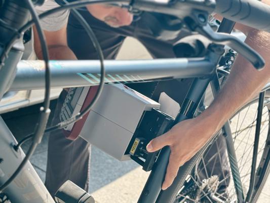 Eine Person hält ein Fahrrad fest, während ein Codiergerät am Rahmen eines abgestellten Rads angebracht wird.