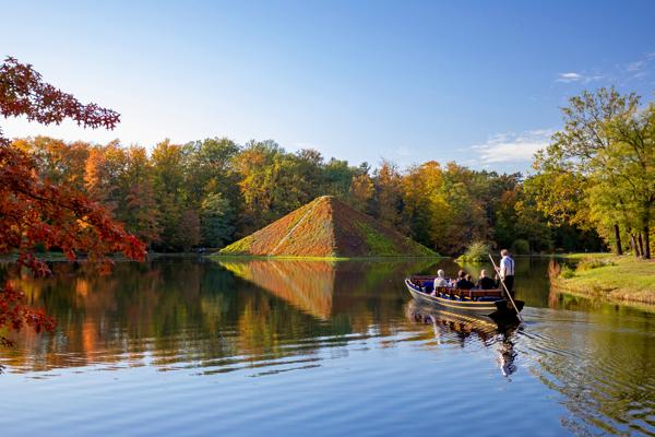 Eine Gondel mit mehreren Personen fährt über den See am Tumulus im herbstlich gefärbten Branitzer Park.