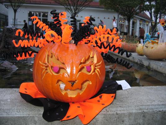 Ein geschnitzter Halloween-Kürbis mit grinsender Fratze liegt auf orange-schwarzem Tuch am Wasserbecken.