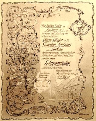 Eine kunstvoll verzierte historische Urkunde mit Kalligrafie, Blumenornamenten und kleinem Gebäudemotiv.