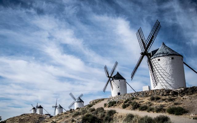 Mehrere weiße Windmühlen stehen auf einem kahlen Hügelkamm unter einem weiten Himmel mit aufziehenden Wolken.