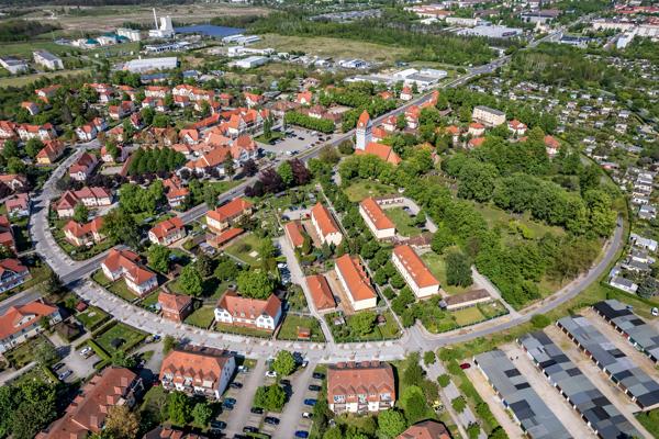Aus der Luft zeigt sich die Gartenstadt Marga mit ringförmigen Straßen, roten Dächern, Grünflächen und dem zentralen Platz.