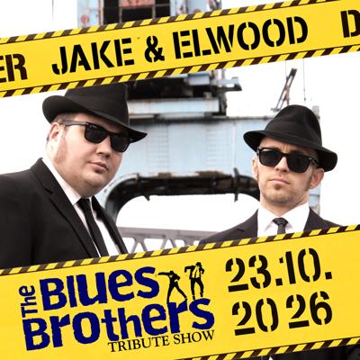 Zwei Männer in schwarzen Anzügen, Hüten und Sonnenbrillen stehen vor gelb-schwarzem Streifenband mit „The Blues Brothers Tribute Show“.