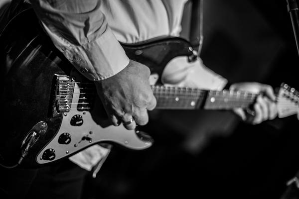 Nahaufnahme einer schwarzen E-Gitarre, auf der eine Hand die Saiten spielt, während die andere den Hals greift.