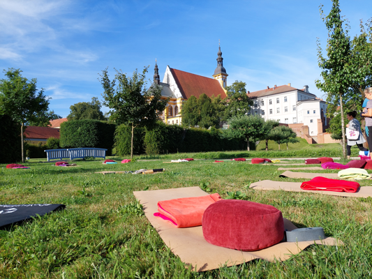 Auf der Wiese im Klostergarten Neuzelle liegen Yogamatten und Kissen vor barocker Kulisse für Klangyoga an einem warmen Sommerabend unter freiem Himmel.