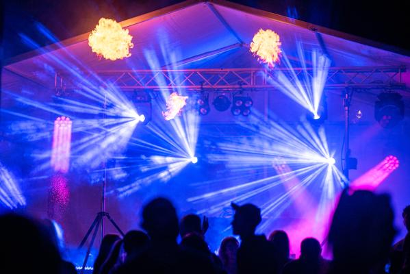 Bunte Lichtstrahlen, Nebel und eine Bühne im Festzelt beleuchten die Silhouetten des Publikums bei einer Abendparty.