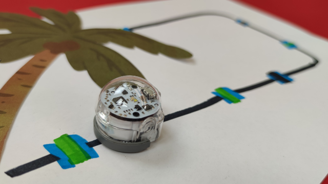 Ein kleiner transparenter Roboter steht auf einer gemalten Insel mit Palme und blau-schwarzer Linie auf weißem Papier.