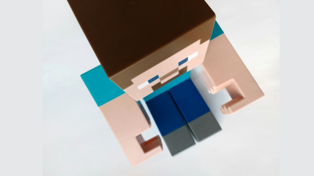 Von oben zu sehen ist eine blockige Minecraft-Figur mit braunem Haar, blauem Shirt und blauer Hose auf hellem Hintergrund.