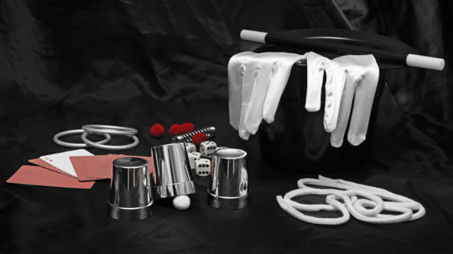 Auf schwarzem Stoff liegen ein Zylinder mit weißen Handschuhen, ein Zauberstab, Karten, Würfel, Seile und rote Bälle.