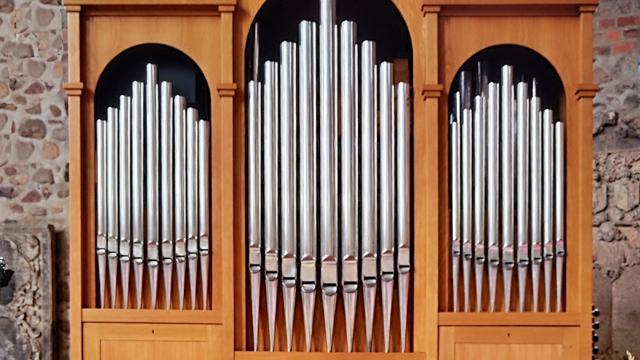 Vor der steinernen Wand stehen silberne Orgelpfeifen in einem hölzernen Gehäuse, passend zur Orgelmusik im Dom St. Marien zu Fürstenwalde.