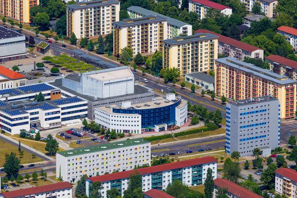 Aus der Vogelperspektive sind Wohnblöcke, ein rundes zentrales Gebäude und baumgesäumte Straßen zu sehen.