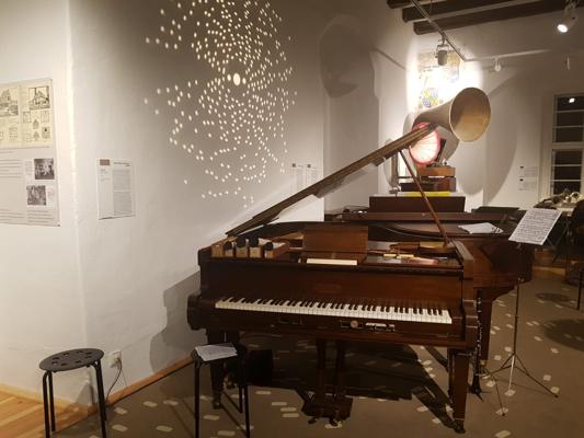 Im Musikmuseum auf Burg Beeskow steht ein mechanischer Flügel neben einem Grammophon und verweist auf „Der unsichtbare Pianist im Kaffeehaus“.