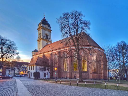 Die Backsteinkirche St. Marien steht an einem Platz mit Kopfsteinpflaster, beleuchtet vom warmen Abendlicht.