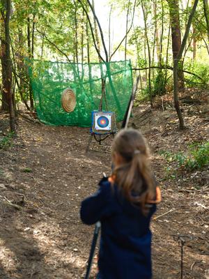 Ein Kind zielt beim Bogenschießen im Wald auf eine Zielscheibe, passend zum Herbstferiencamp am Deulowitzer See mit Naturerlebnis und Gemeinschaft.