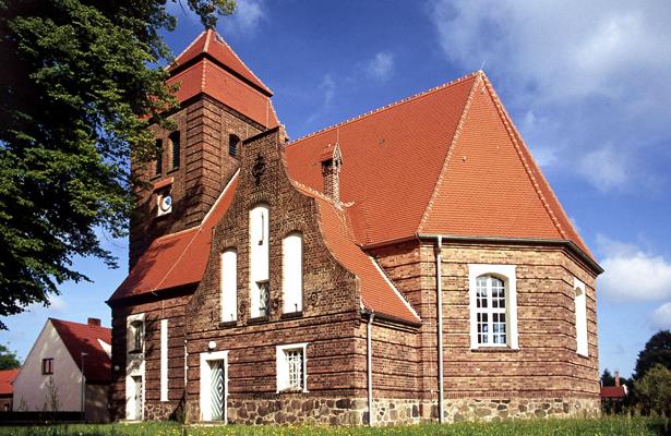 Die Dorfkirche Pinnow mit rotem Ziegeldach und Backsteinfassade steht unter blauem Himmel und verweist auf die SommerMusik in Pinnow.