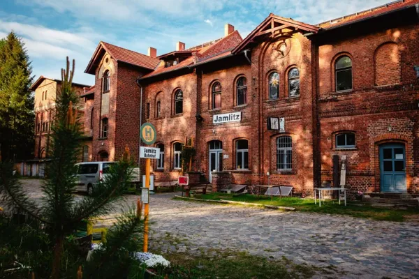 Das Backsteinbahnhofsgebäude in Jamlitz zeigt eine breite Fassade, historische Giebel und ein Schild mit dem Ortsnamen.