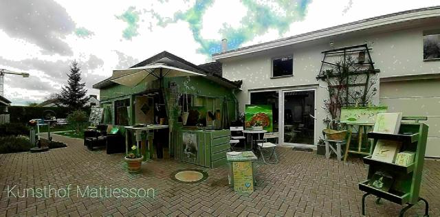Im Innenhof des Kunsthofs Mattiesson stehen grüne Kunstobjekte, Staffeleien und kleine Tische vor dem Gebäude.