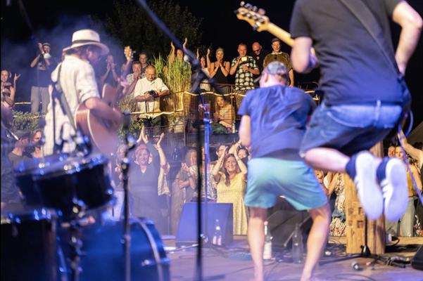 Beim Festival „Liederlauschen am Rand“ spielt eine Band unter freiem Himmel, während das Publikum in Zollbrücke begeistert applaudiert und mitfeiert.