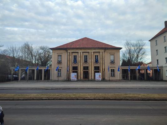 Vor dem Theater in Guben hängen blaue Fahnen, während die Kinderfilmclub-Eröffnungsparty mit Rally Ewersbach am Gebäude angekündigt wird.