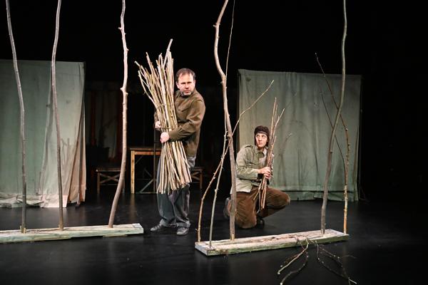 Zwei Darsteller von Daylin Leach in WOYZECK von Büchner stehen auf der dunklen Bühne zwischen dünnen Ästen und tragen Reisigbündel im Spiel.