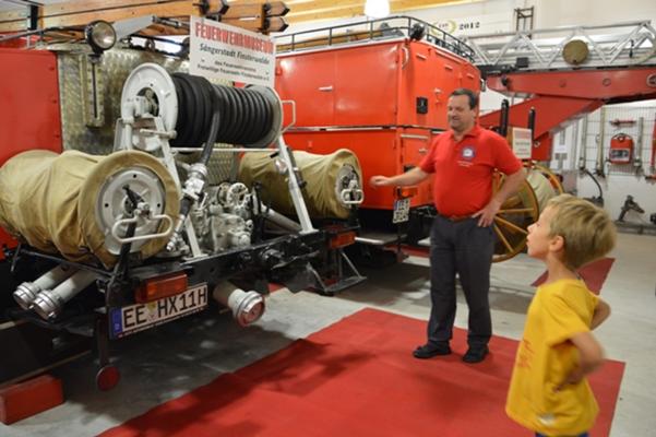 Ein Museumsführer erklärt einem Kind historische Feuerwehrfahrzeuge im Feuerwehrmuseum Finsterwalde, Foto: Pressestelle Finnstrwalde, Lizenz: Pressestelle Finsterwalde