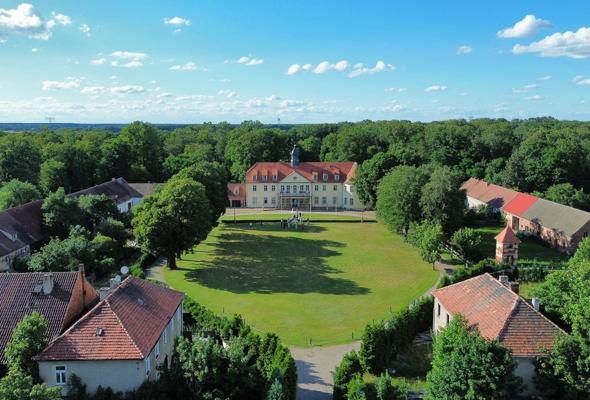 Luftaufnahme vom Schloss Grochwitz mit rotem Dach, großer Wiese, Nebengebäuden und dichtem Wald unter blauem Himmel., Foto: Bettina Unterkofler, Lizenz: Bettina Unterkofler