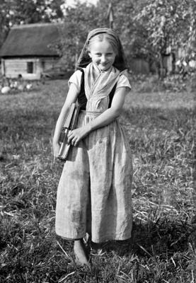 Ein Schulmädchen in wendischer Tracht steht mit Schulbüchern in der Hand barfuß auf einer Wiese. Altes schwarz-weiß Foto, Foto: Denis Galloway, Lizenz: Ethnographical Museum of Transylvania, Romania