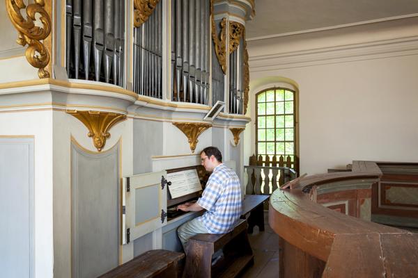 Mann spielt auf der Kirchenorgel mit großen Orgelpfeifen und goldenen Verzierungen; rechts ein hohes Fenster., Foto: Andreas Franke, Lizenz: Andreas Franke