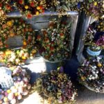 Am Stand hängen und liegen farbenfrohe Kränze und Trockenblumen aus Blüten, Beeren und Samen in vielen Formen.