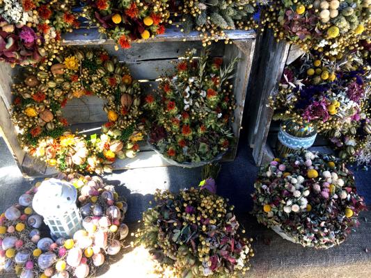 Am Stand hängen und liegen farbenfrohe Kränze und Trockenblumen aus Blüten, Beeren und Samen in vielen Formen.