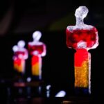 Mehrere gläserne Figuren in Rot, Gelb und Weiß stehen vor dunklem Hintergrund, eine große Figur im Vordergrund.