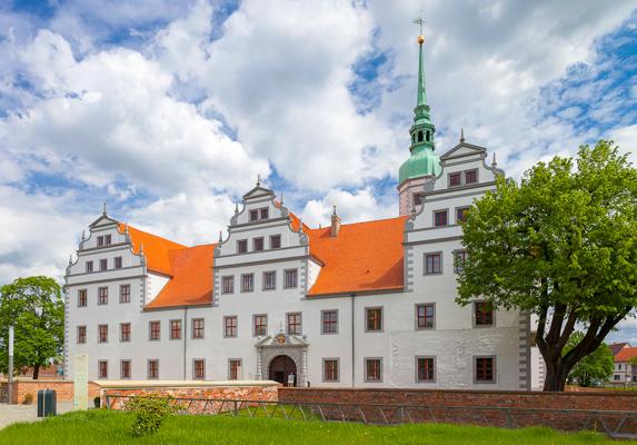 Weißes Schloss mit roten Ziegeldächern, Stufengiebeln und grünem Turm vor wolkigem Himmel; Baum im Vordergrund., Foto: Andreas Franke, Lizenz: Andreas Franke
