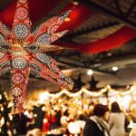 Ein leuchtender Stern hängt vor festlich beleuchteten Ständen, während Besucher durch die Messehalle schlendern.